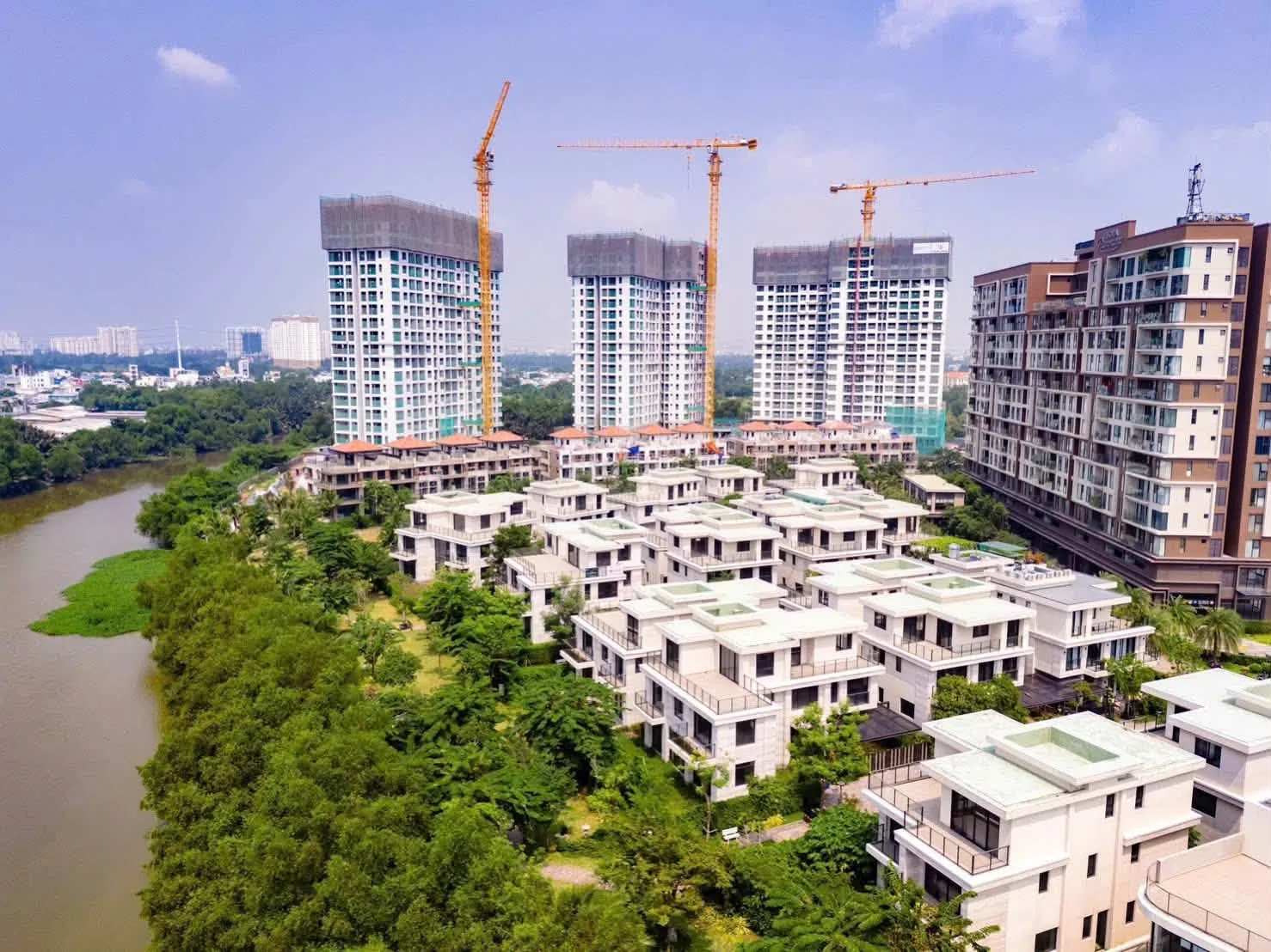 Ba tháp Trellia Cove cao 20 tầng với cần cẩu tháp và dãy nhà thấp tầng ven kênh tại Mizuki Park